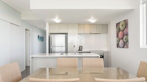 A modern kitchen with white cabinets, a stainless steel refrigerator, and a white island with seating. - Holborn at Central (Townsville)