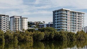 A modern apartment complex with multiple high-rise buildings, a calm lake in the foreground, and a clear sky. - Holborn at Central (Townsville)