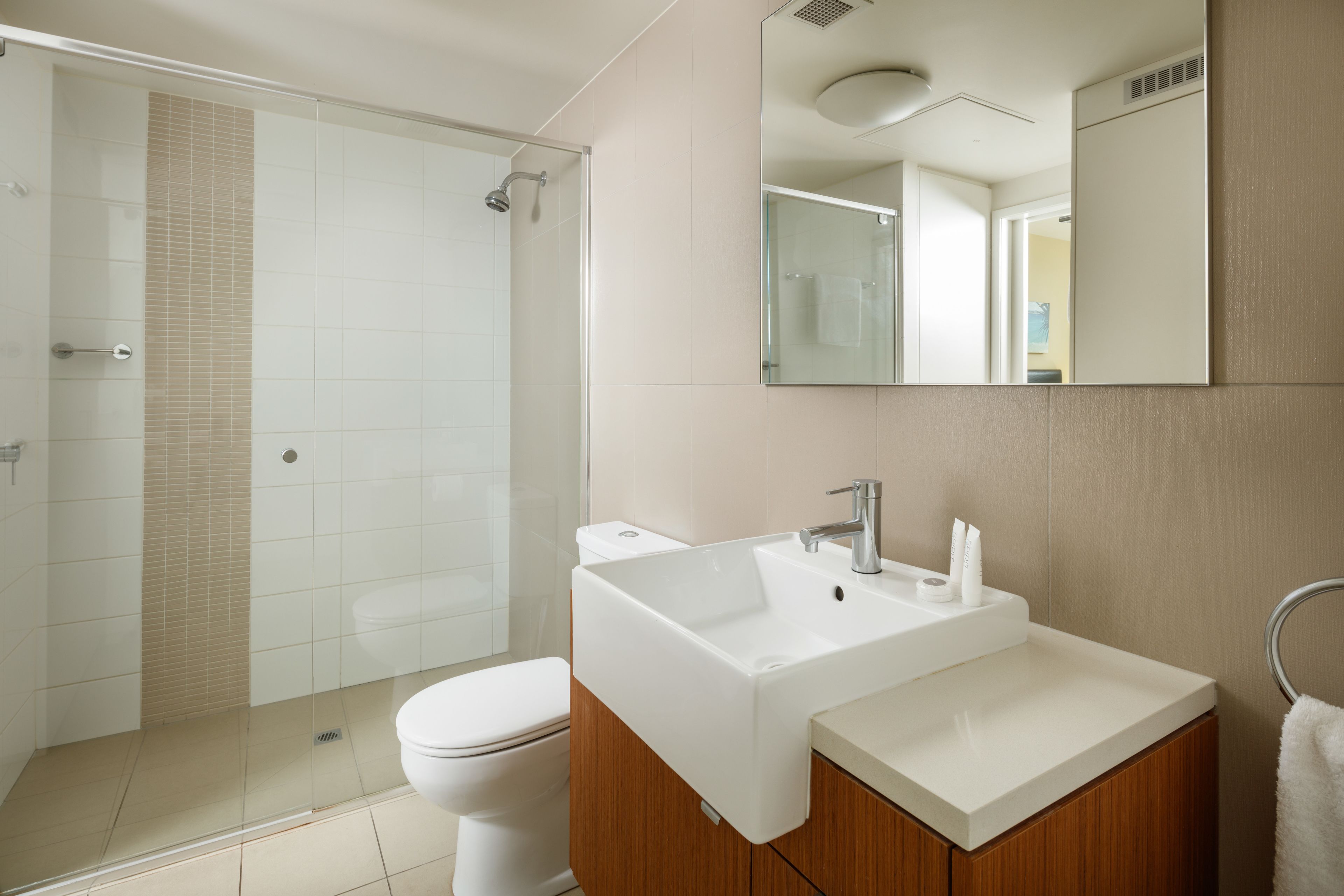A modern bathroom with a glass-enclosed shower, a white sink, and a wooden vanity.