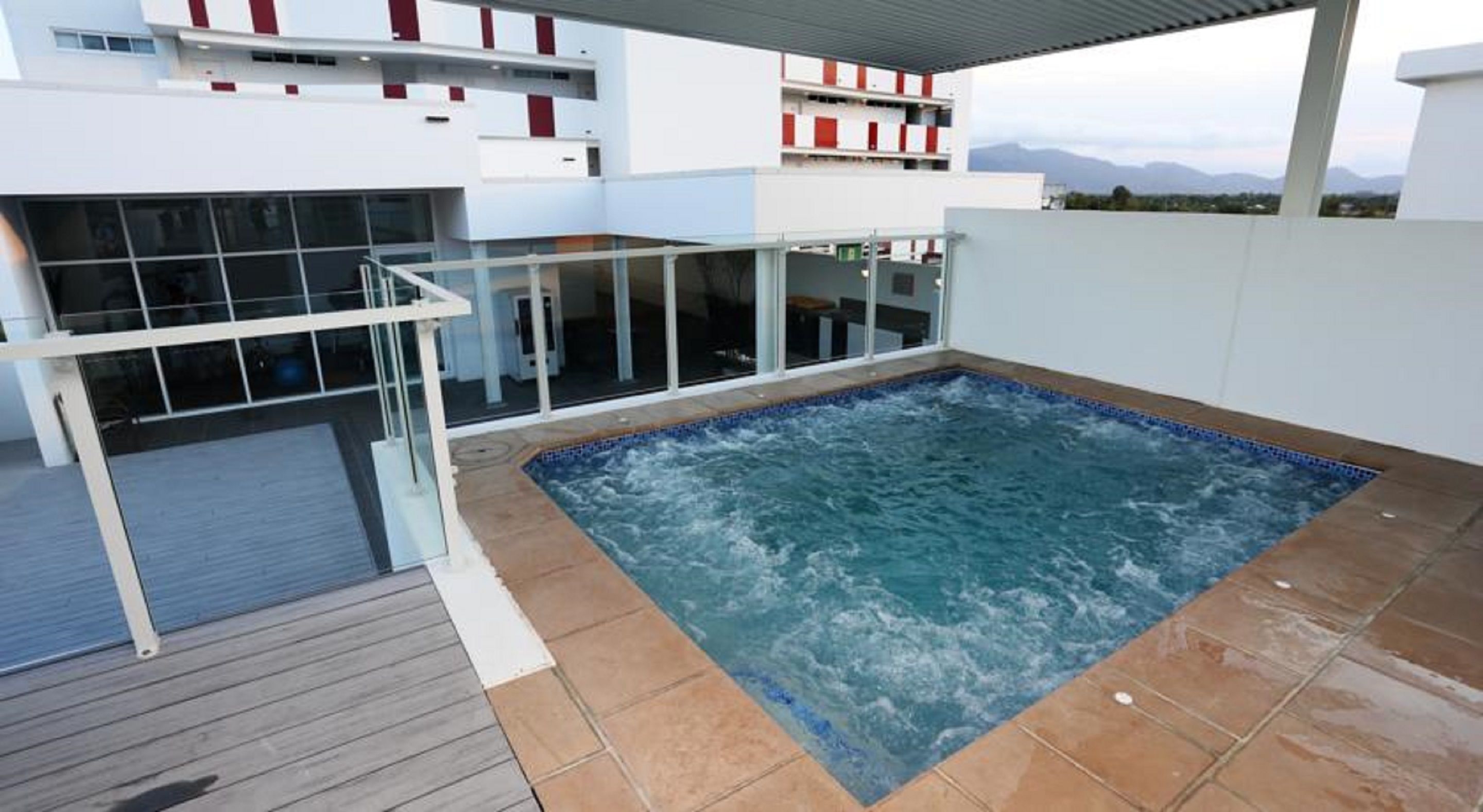 Área de piscina no terraço com hidromassagem, guarda-corpos de vidro e vista para montanhas.
