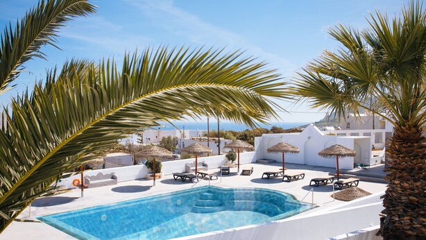 A pool area with lounge chairs, umbrellas, and a clear view of the sea. - Nikos Hotel (Santorini)