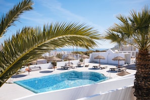 A pool area with lounge chairs, umbrellas, and a clear view of the sea. - Nikos Hotel (Santorini)