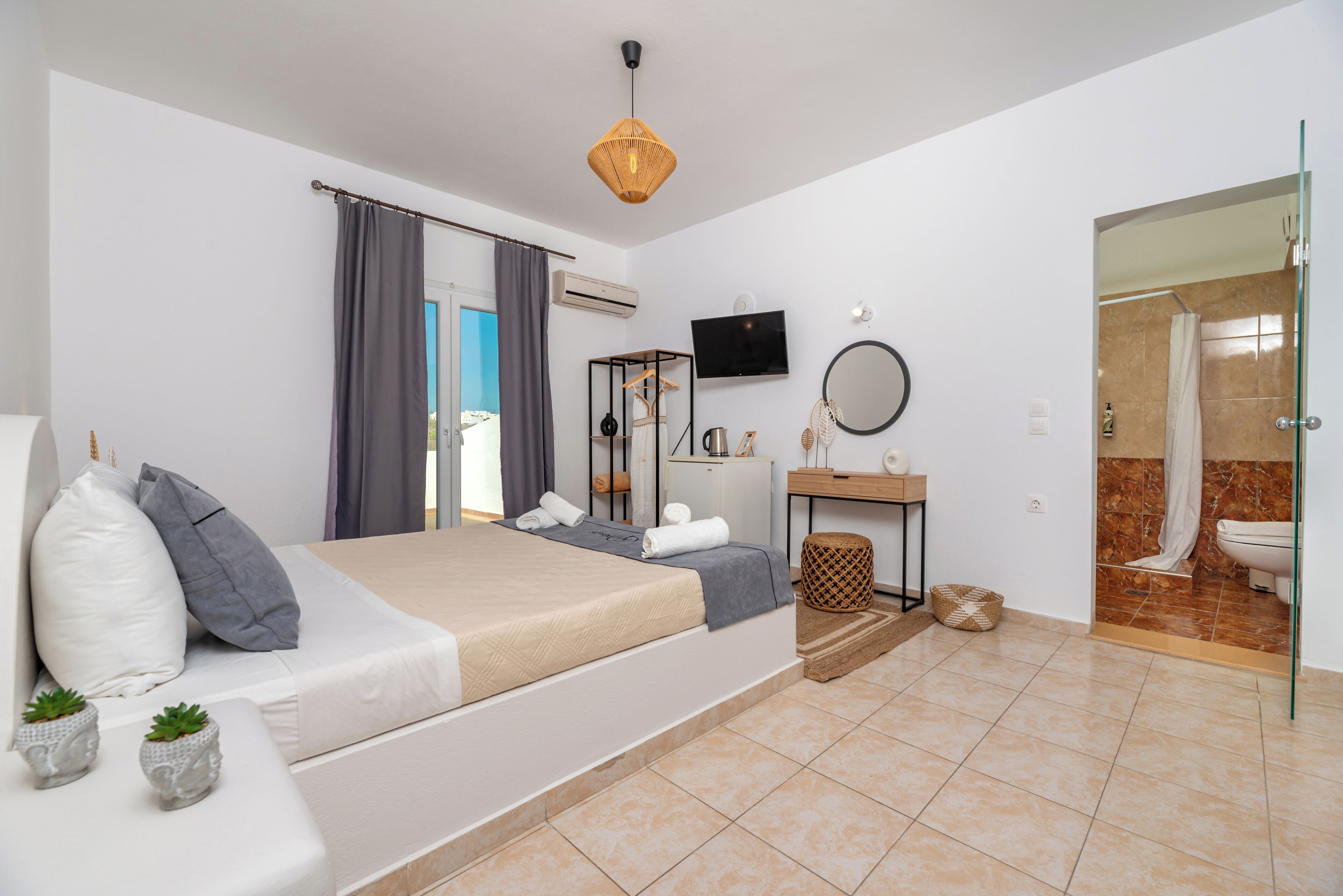 Ein modernes Schlafzimmer mit Bett, Nachttisch, Fernseher und einem Badezimmer mit Dusche und Toilette.