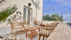 An outdoor seating area with wooden furniture and a stone wall. - Nikos Hotel (Santorini)