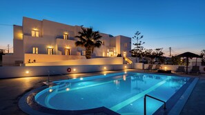 A modern hotel with a swimming pool, outdoor seating, and a well-lit facade. - Nikos Hotel (Santorini)