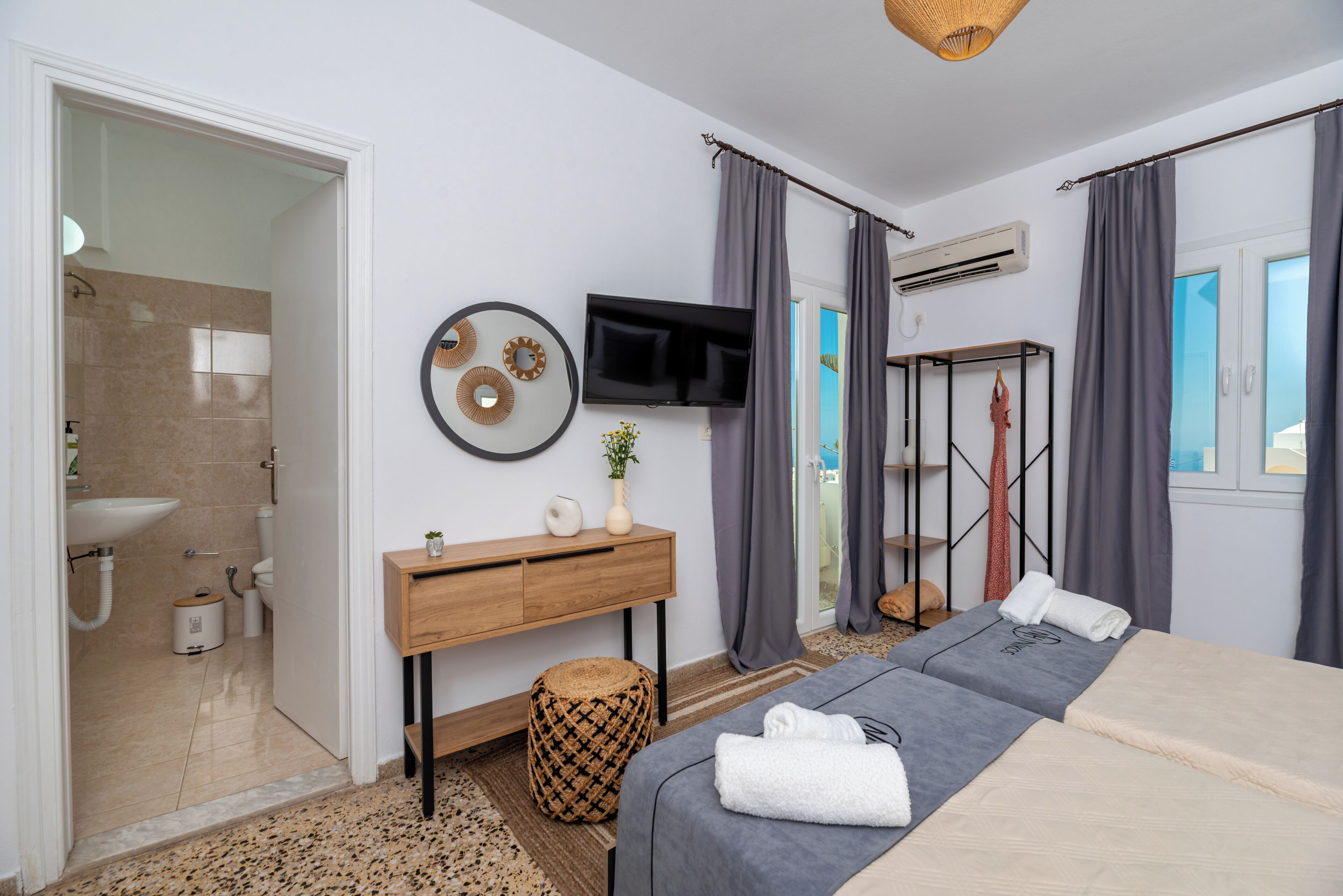 A modern bedroom with a bed, a TV, a wooden console, and a bathroom visible through an open door.