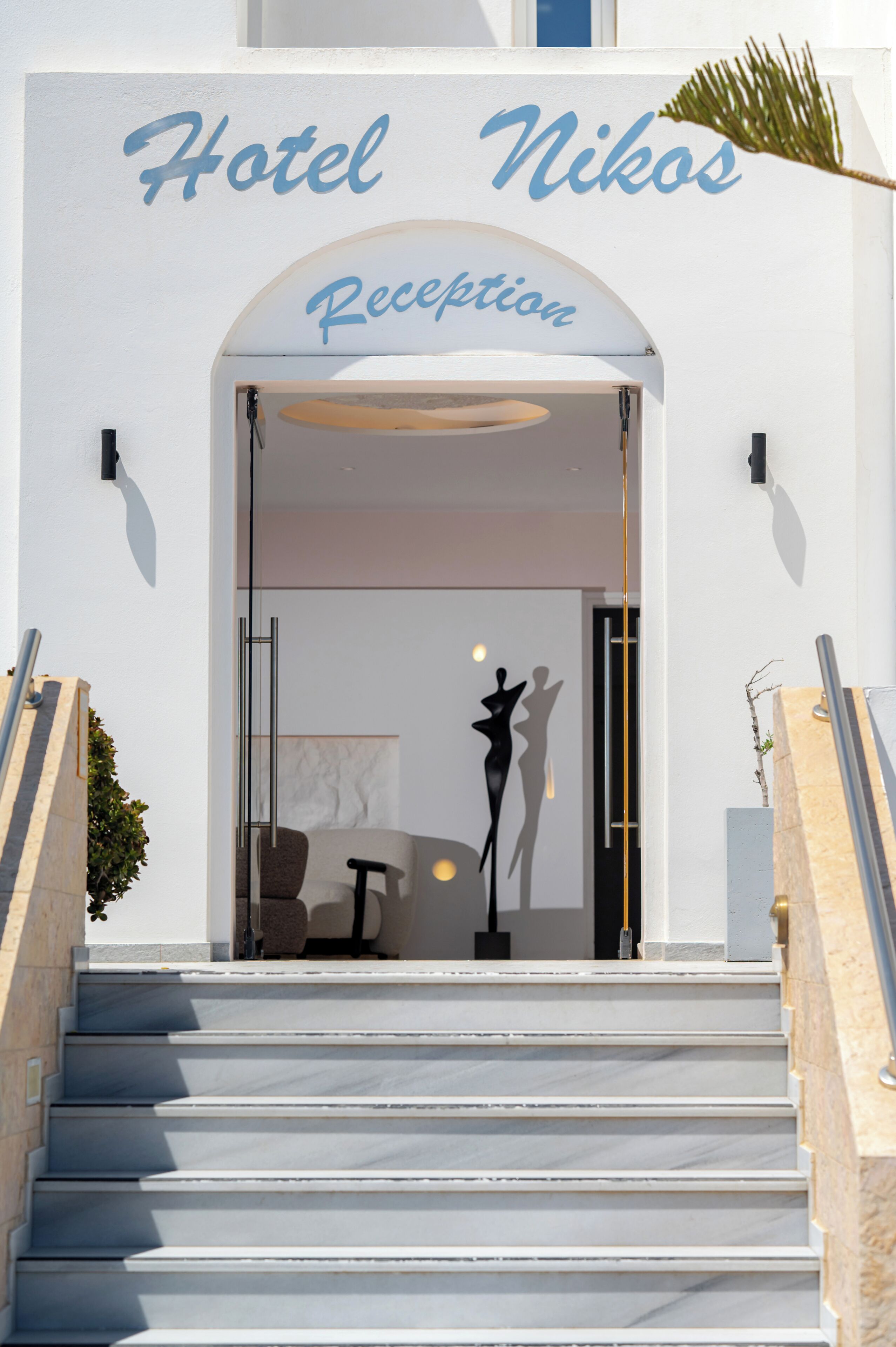 A hotel entrance with a reception desk, a staircase, and a palm tree.