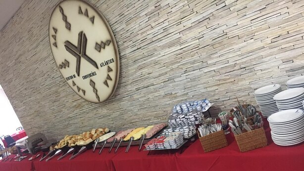 Montaje de bufé con diferentes alimentos y utensilios, un reloj en la pared y un mantel rojo.