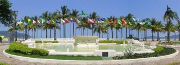 A landscaped area with a central fountain, palm trees, and multiple flags.