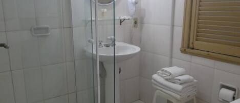 A bathroom with a glass shower enclosure, a sink, a toilet, and a small stool.