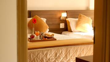 Une chambre d’hôtel avec deux lits, une table de chevet sur laquelle se trouve un plateau de petit-déjeuner, un vase avec une fleur et une lampe fixée au mur.