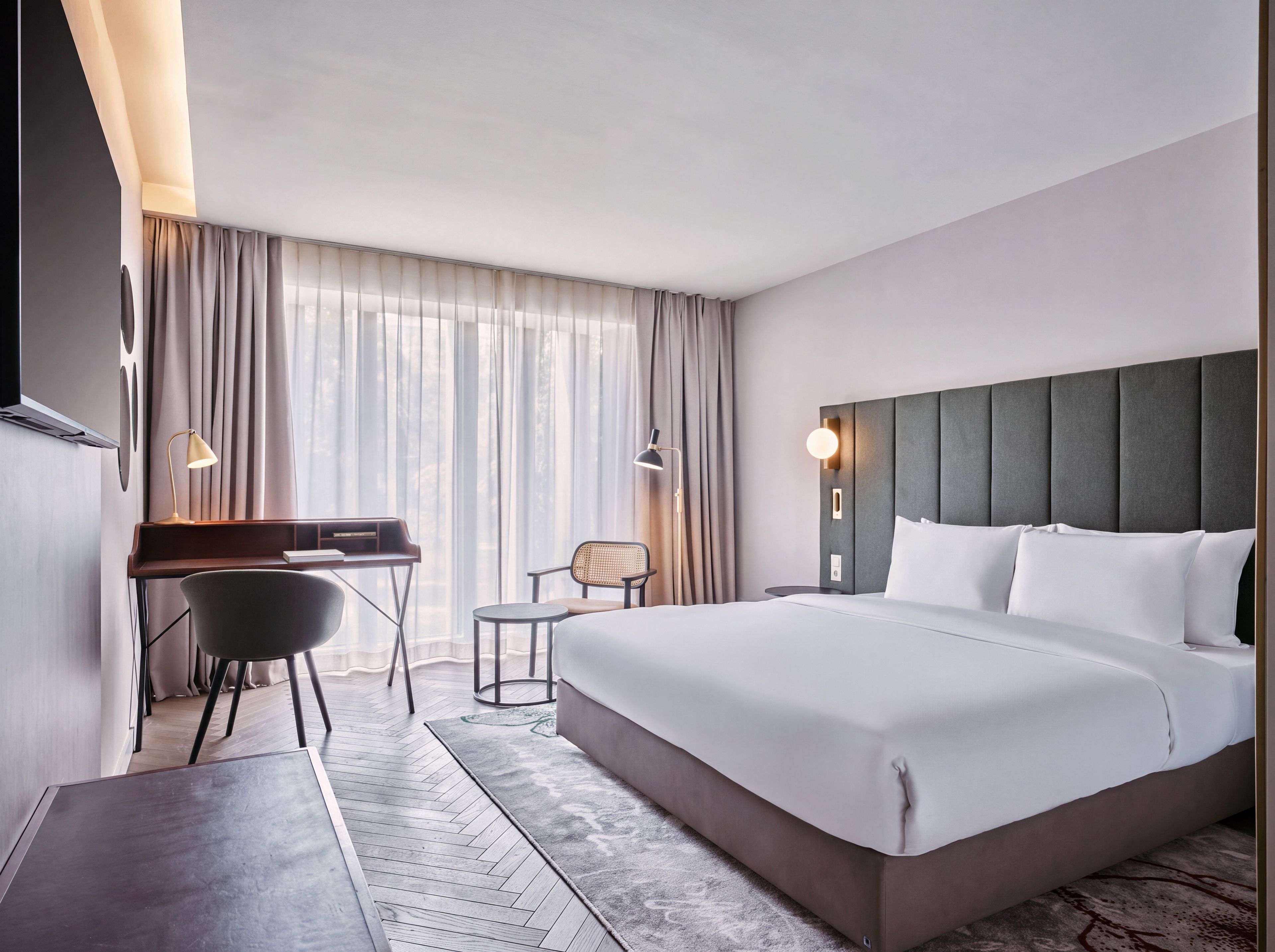 A hotel room with a large bed, a desk, a chair, and a window with curtains.