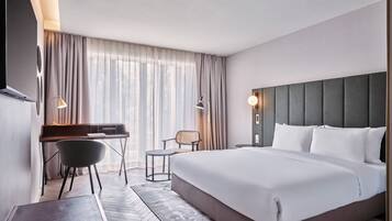 A hotel room with a large bed, a desk, a chair, and a window with curtains.