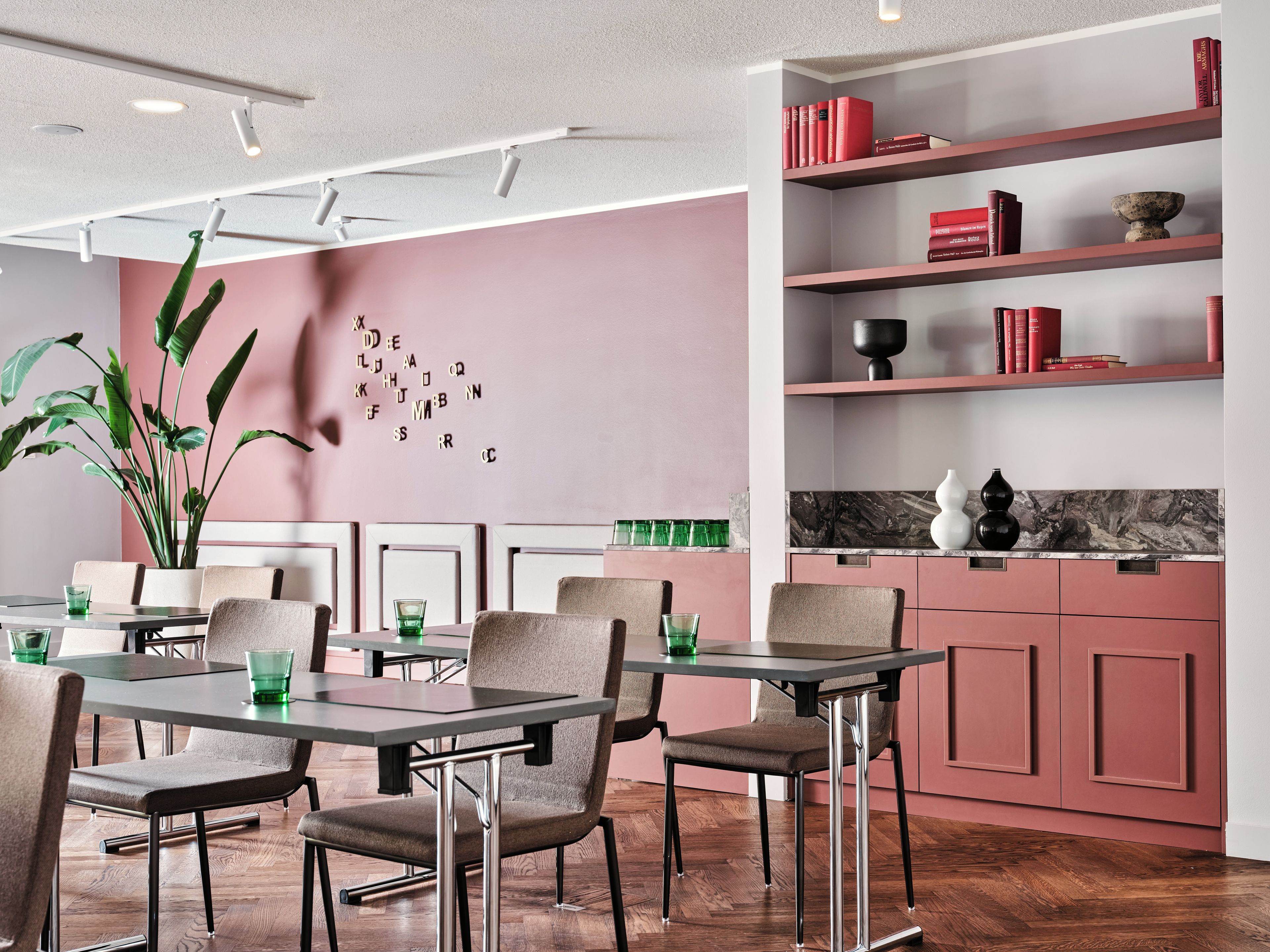 Uma área de refeições moderna com piso de madeira, uma mesa com cadeiras e uma estante com livros e objetos decorativos.