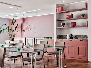 Uma área de refeições moderna com piso de madeira, uma mesa com cadeiras e uma estante com livros e objetos decorativos.