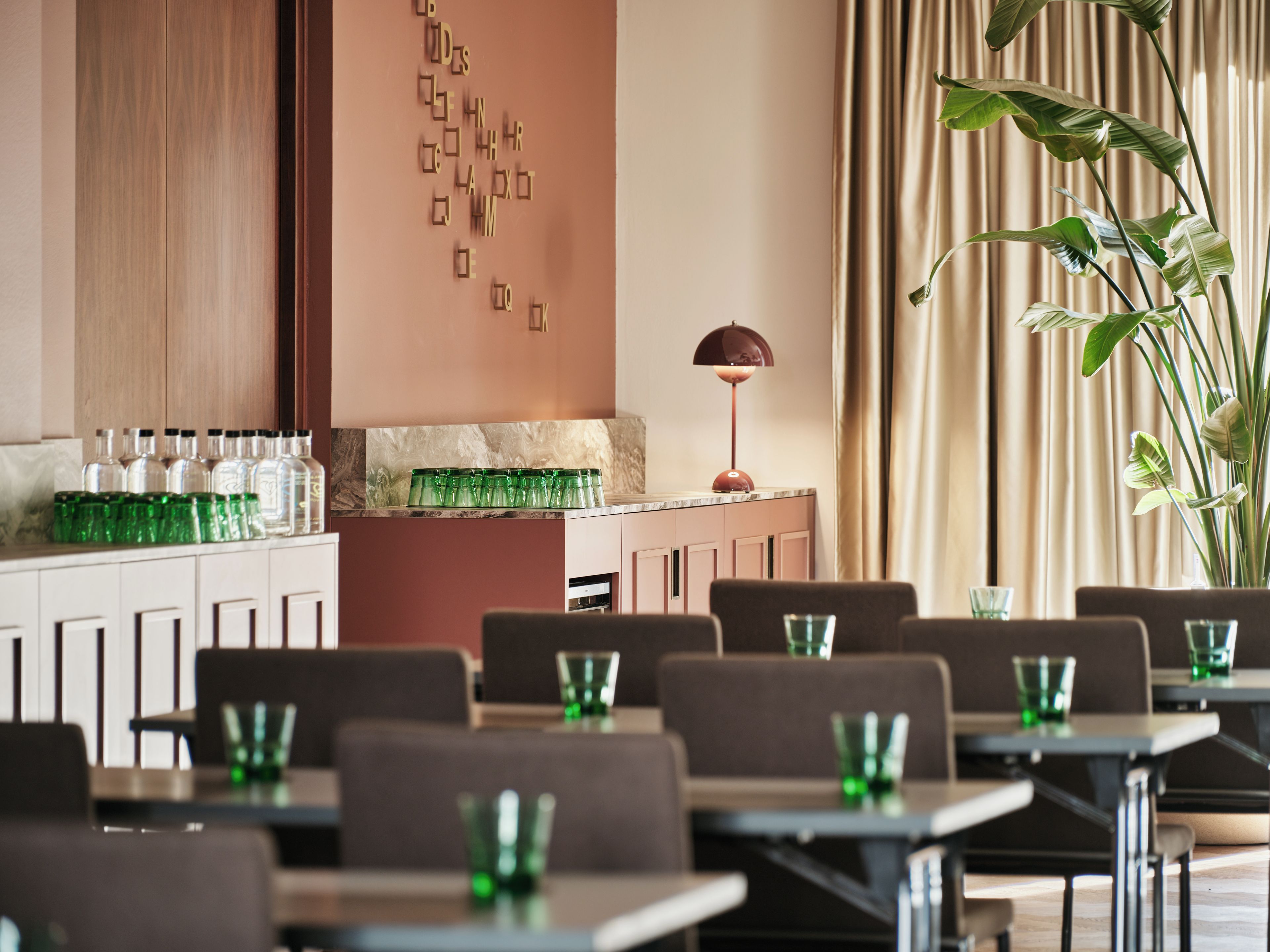 L’intérieur d’un restaurant, avec des tables, des chaises, un bar où sont exposées des bouteilles, et un mur décoratif.