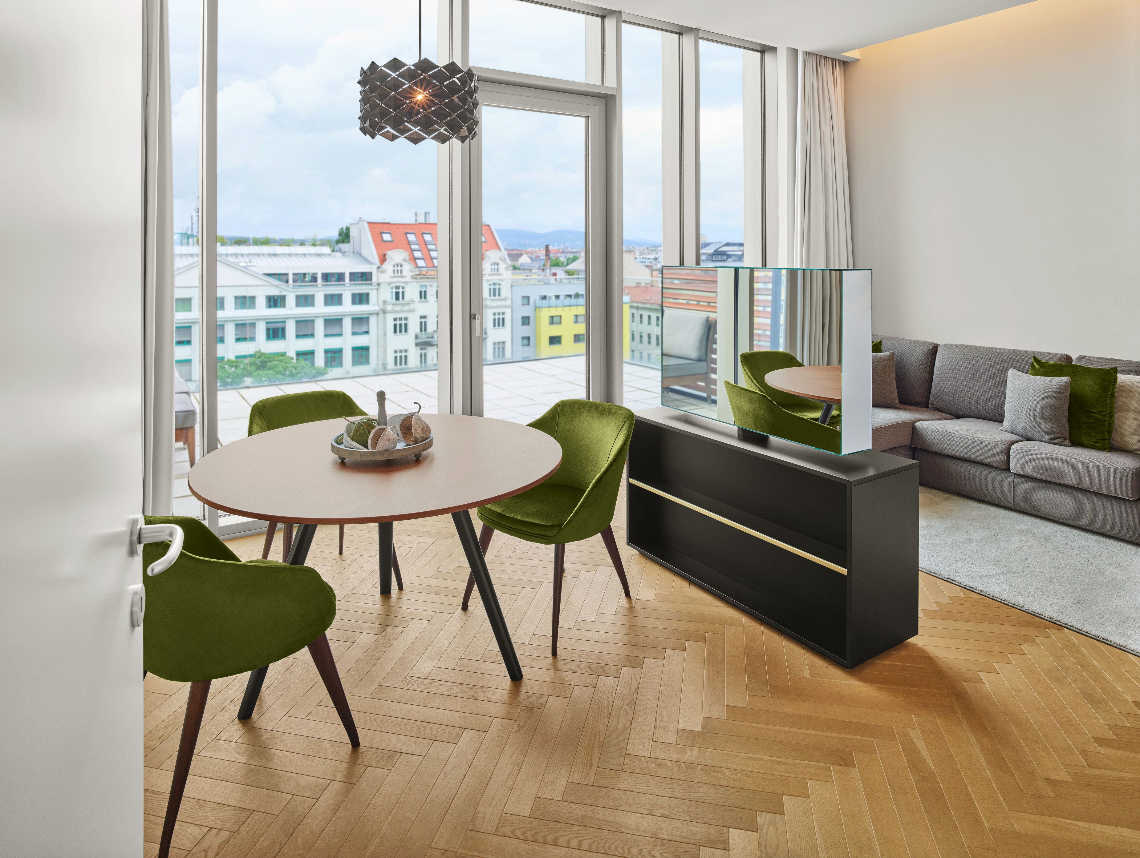 A modern living room with a sofa, a dining table with chairs, and a view of buildings through large windows.