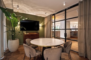 Un comedor moderno con una mesa redonda, seis sillas, un televisor y una planta grande.