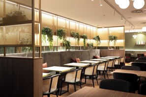 En restaurantindretning med høje borde, polstrede siddepladser og lodrette vægplanter.