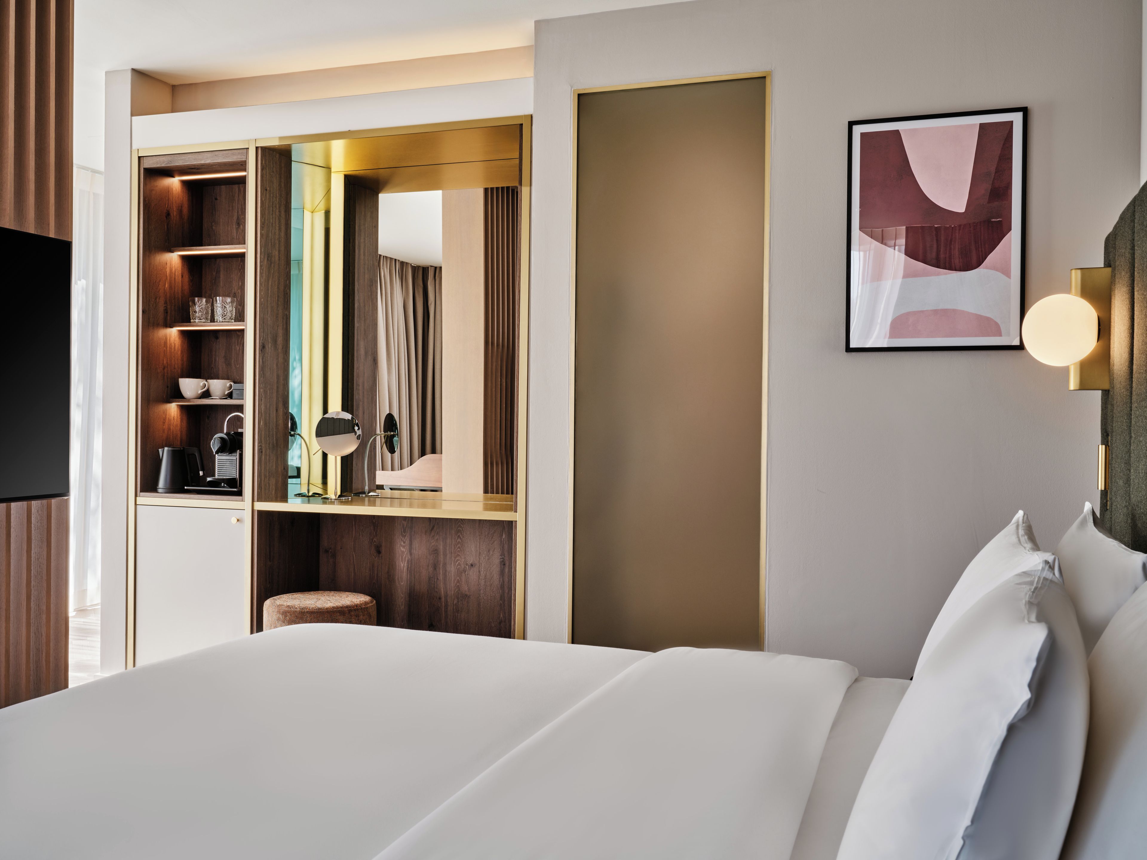 Habitación de hotel con cama, tocador con espejo, máquina de café y estante con tazas y tetera.