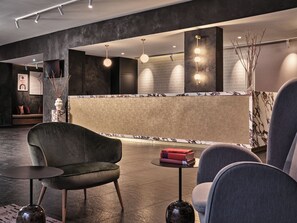 Een moderne lobby met een receptiebalie, een zithoek en decoratieve verlichting.