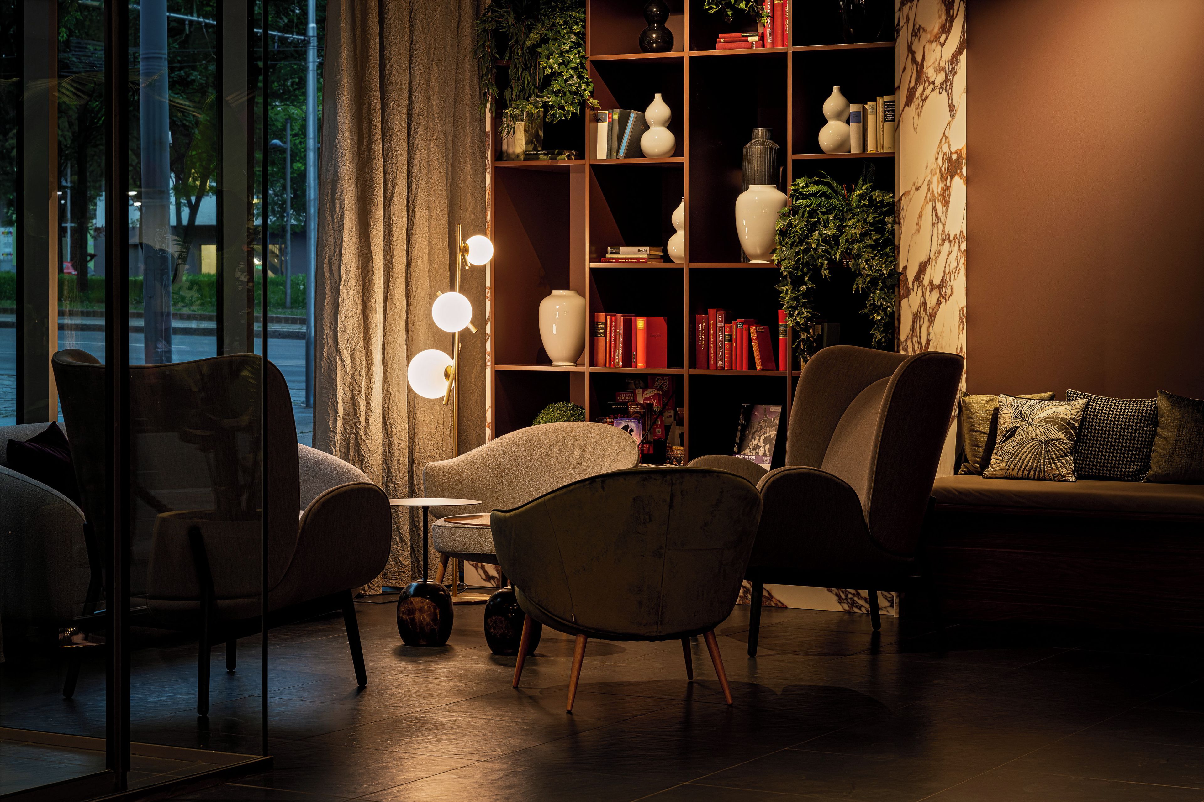 A cozy living room with a sofa, armchairs, a small table, and a bookshelf filled with books and decorative items.