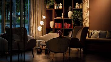 A cozy living room with a sofa, armchairs, a small table, and a bookshelf filled with books and decorative items.