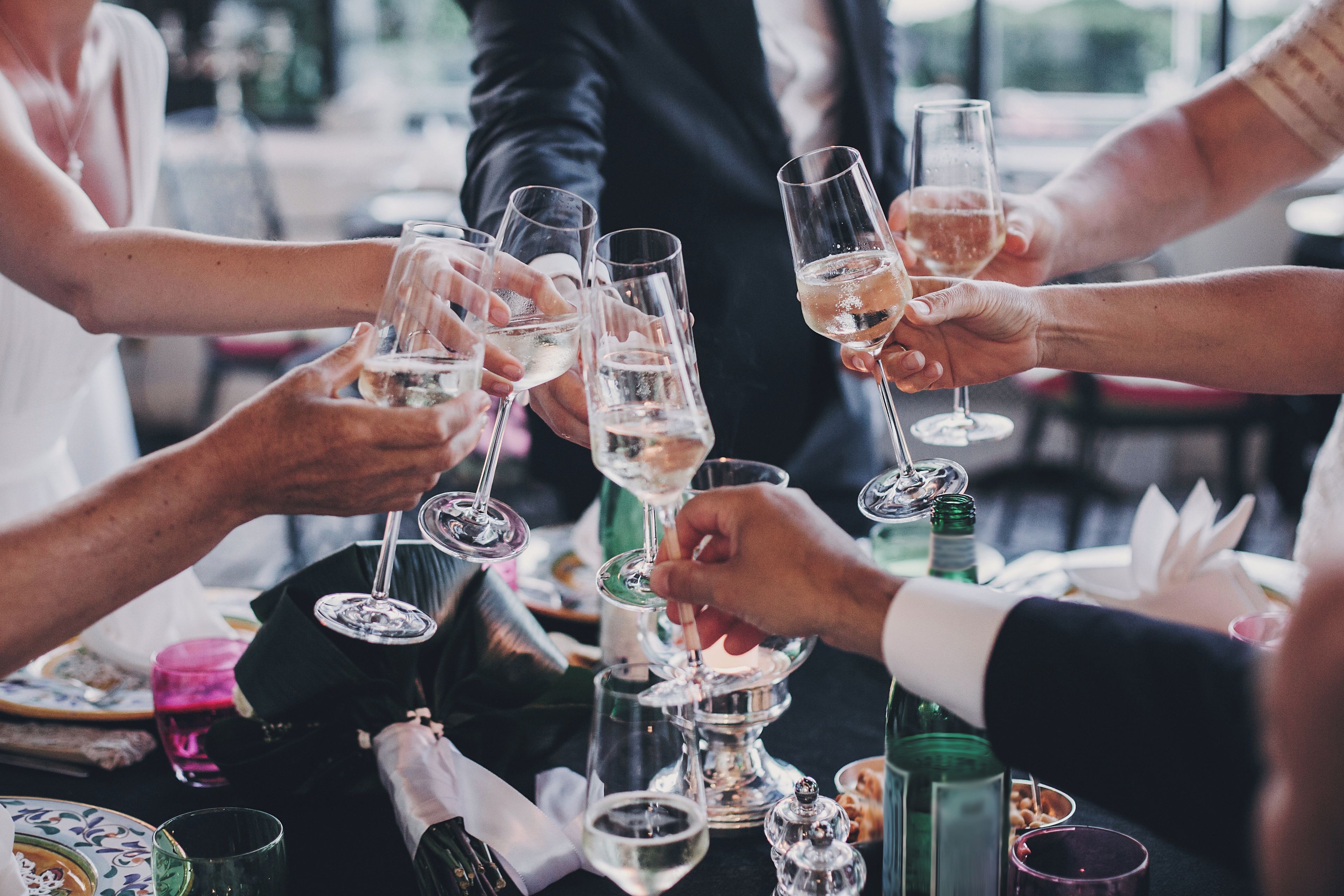 A group of people toasting with wine glasses at a table with various bottles and glasses.