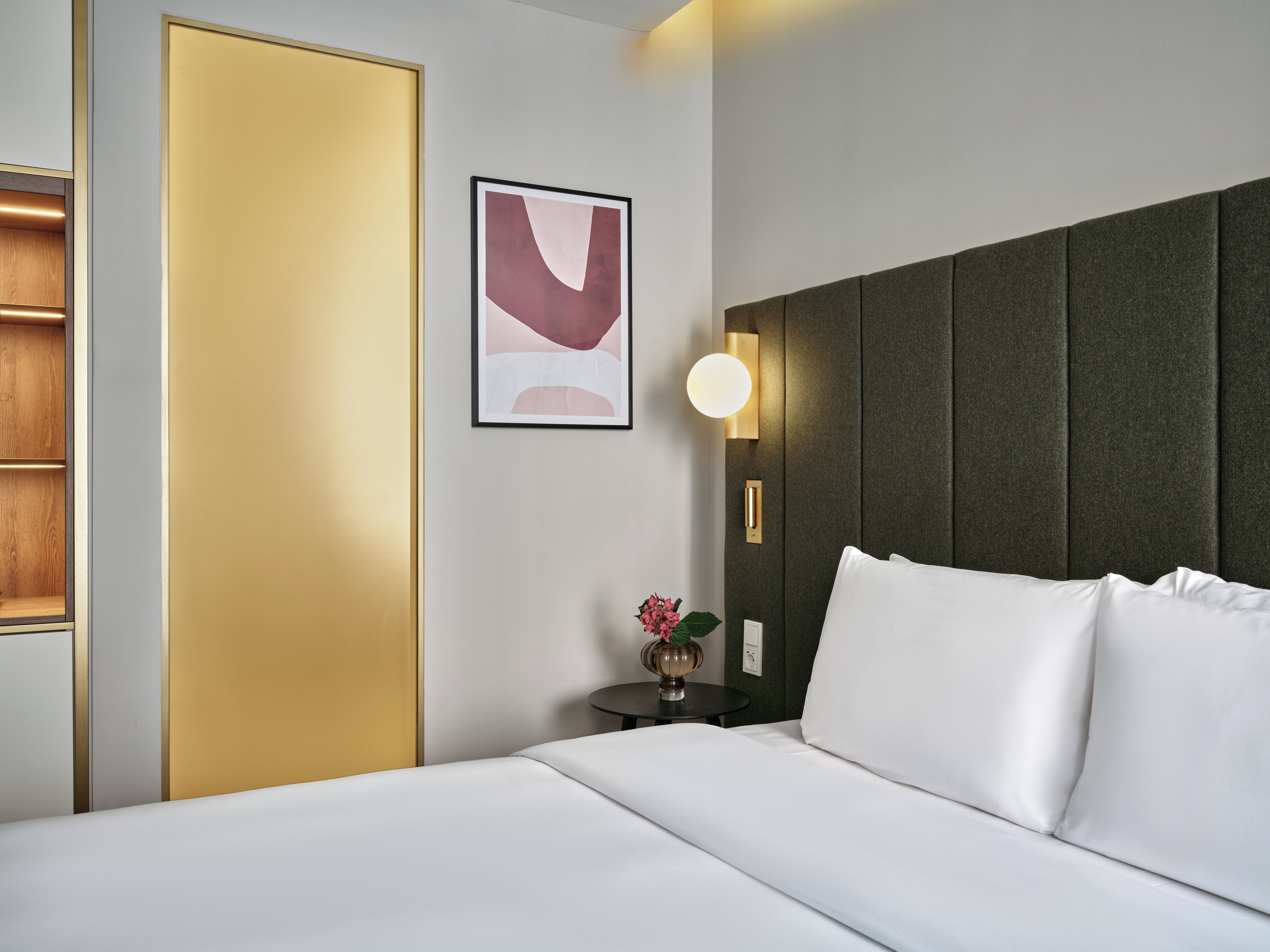 A hotel room with a bed, a nightstand, a wall-mounted light, and a framed picture.