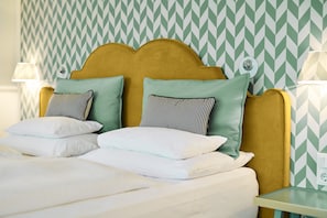 Cama com cabeceira, travesseiros e mesa de cabeceira em quarto com papel de parede estampado.