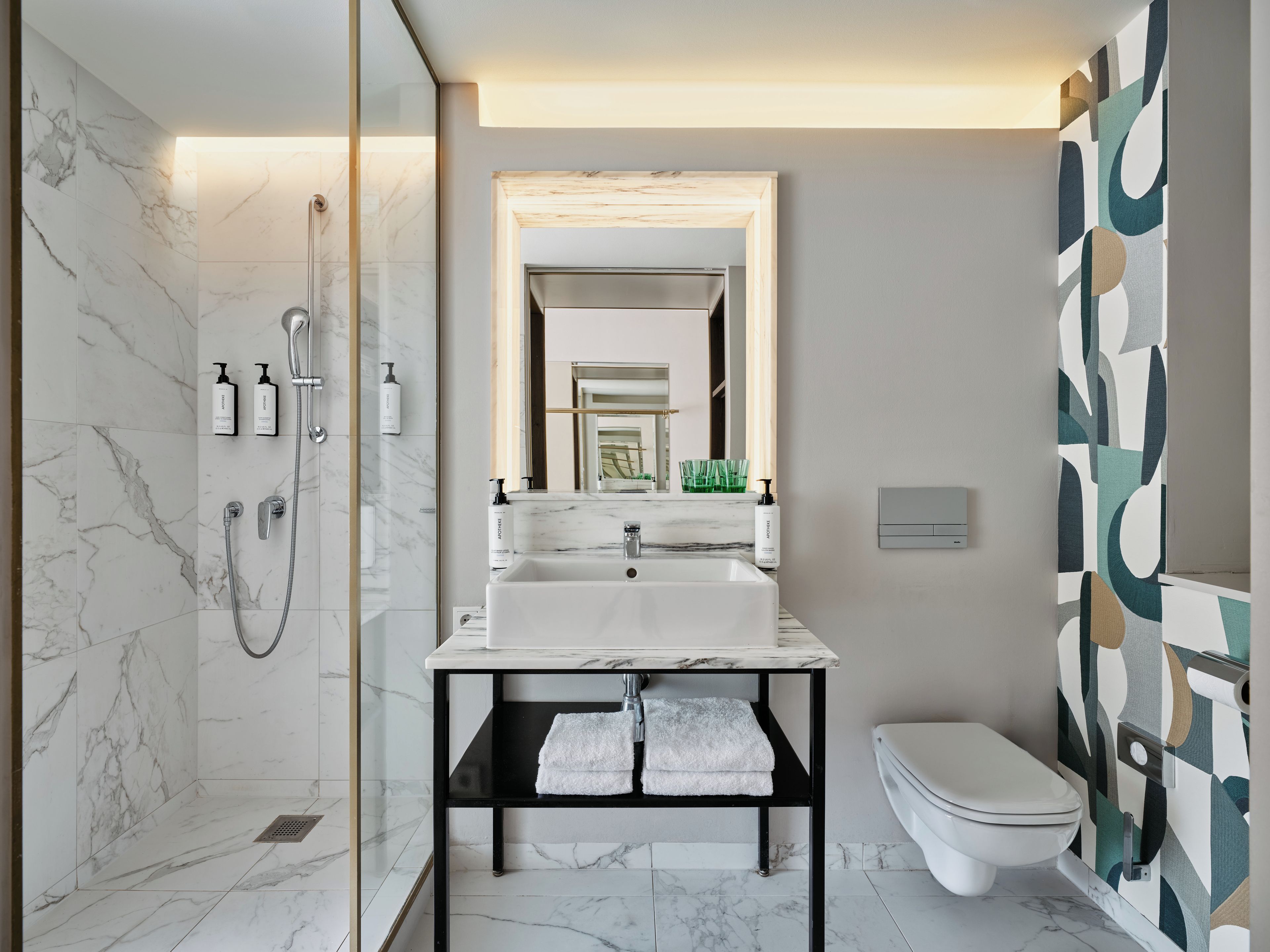 A modern bathroom with a marble shower, a white sink, and a toilet.