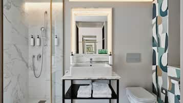 Un baño moderno con ducha de mármol, lavamanos blanco y un inodoro.