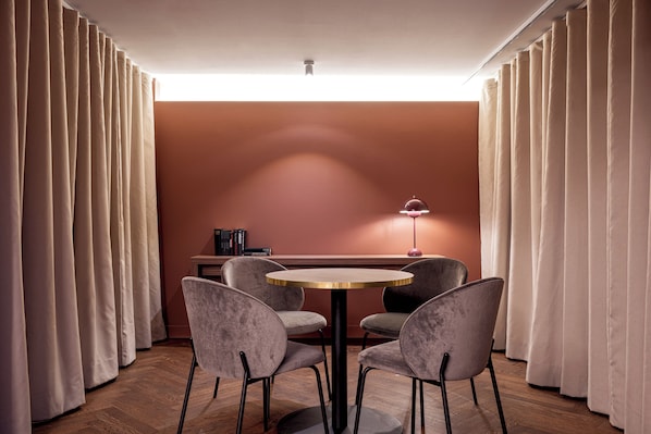A room with a round table, four chairs, a lamp, and a bookshelf. - Crowne Plaza Vienna by IHG (Vienna)