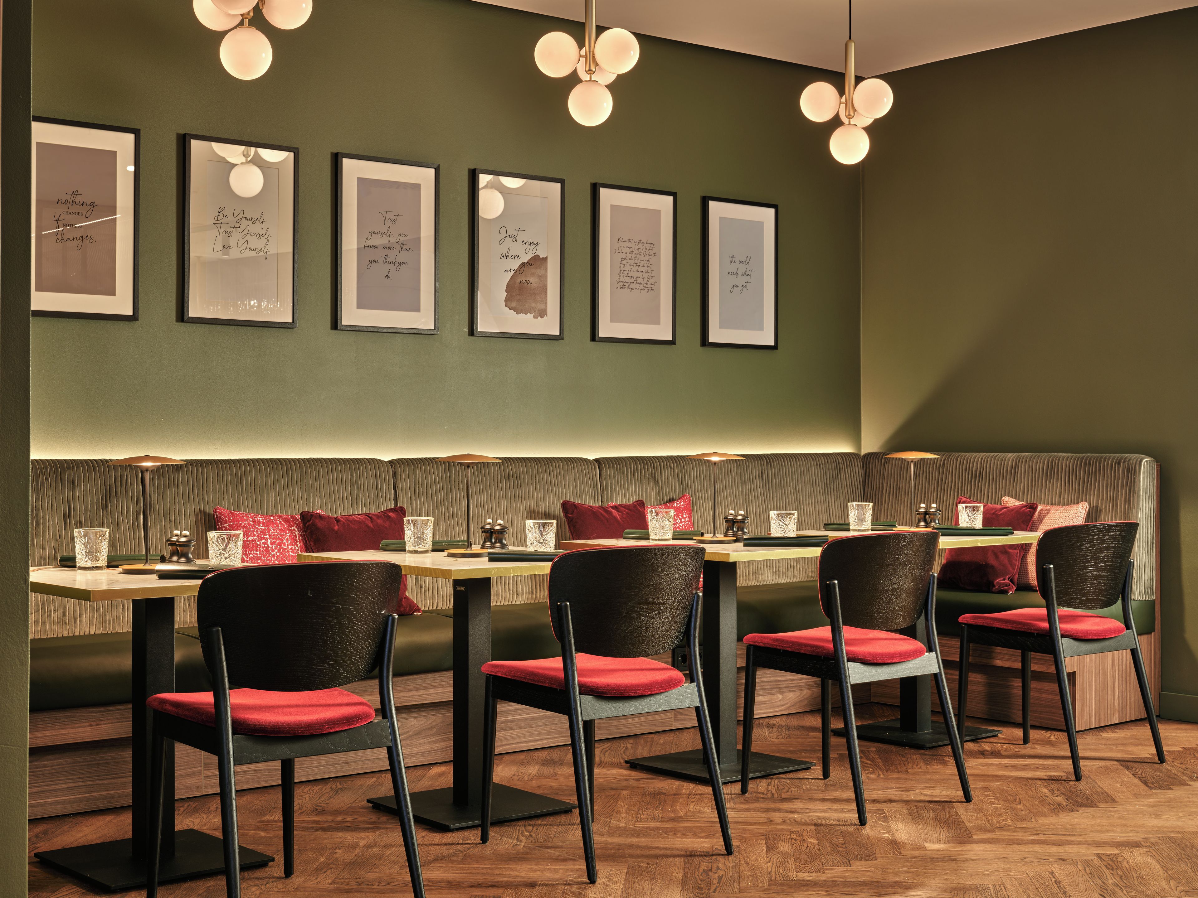 Interior de restaurante com um amplo banco para assentos, mesas com cadeiras e quadros com citações inspiradoras na parede.