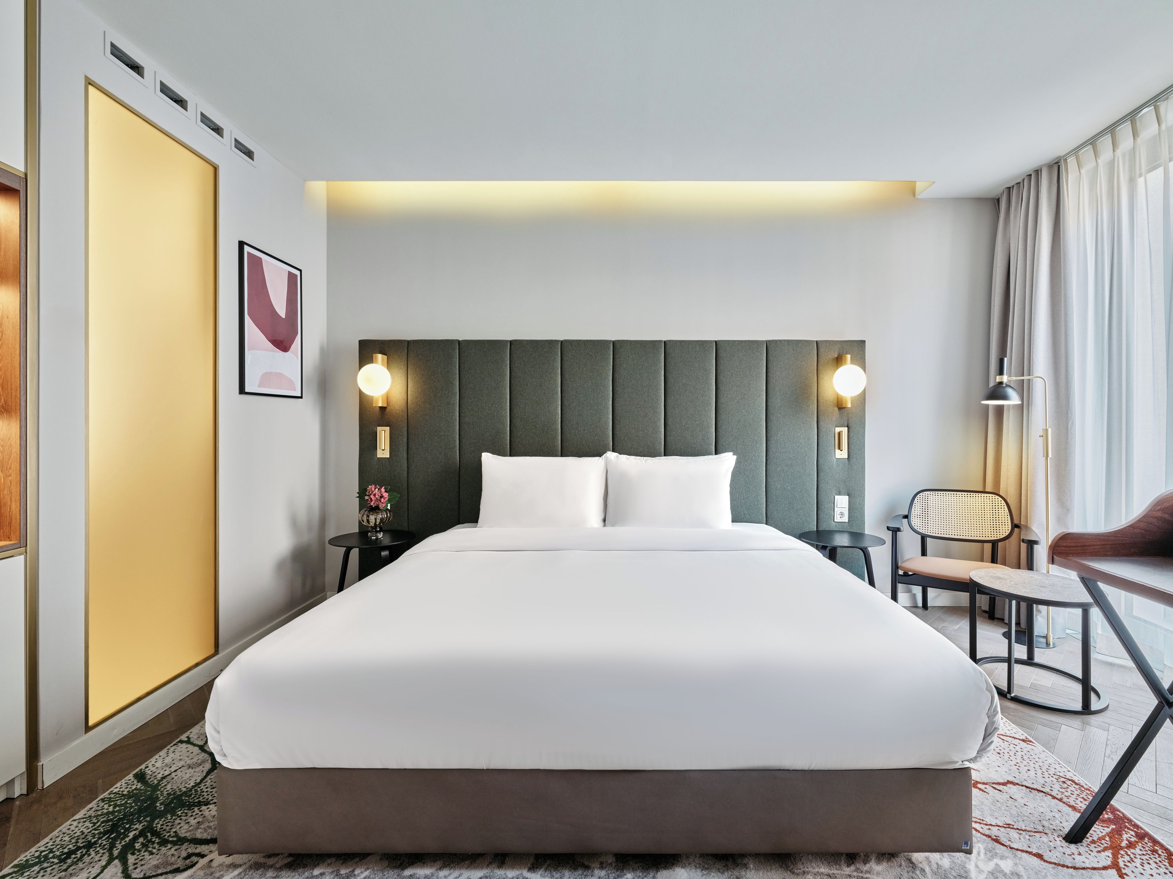 Una habitación de hotel con una cama grande, dos mesitas de noche, una silla, un escritorio y una lámpara.
