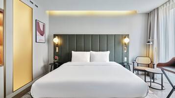 Una habitación de hotel con una cama grande, dos mesitas de noche, una silla, un escritorio y una lámpara.