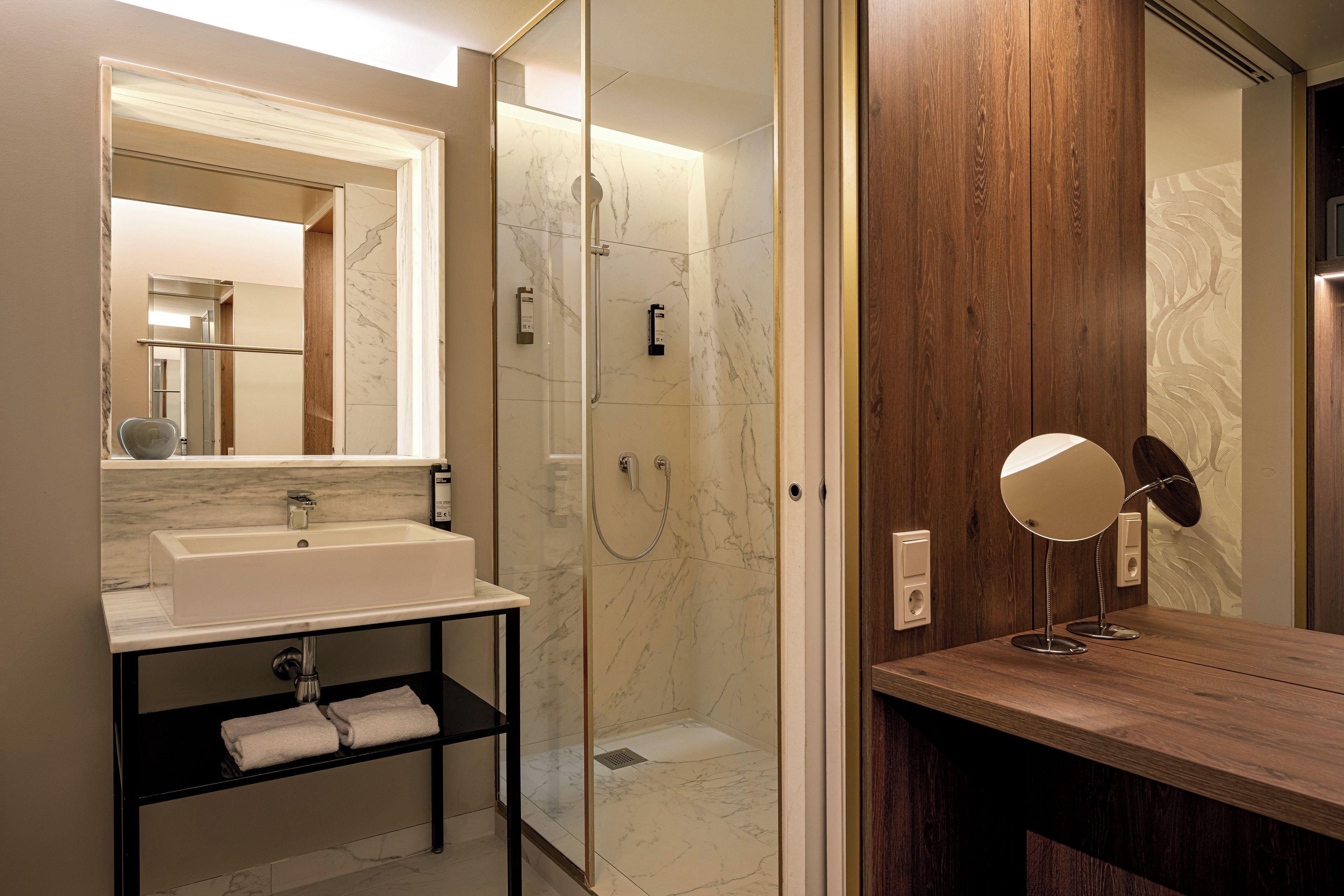 A modern bathroom with a glass-enclosed shower, a wooden vanity, and a marble-tiled sink.