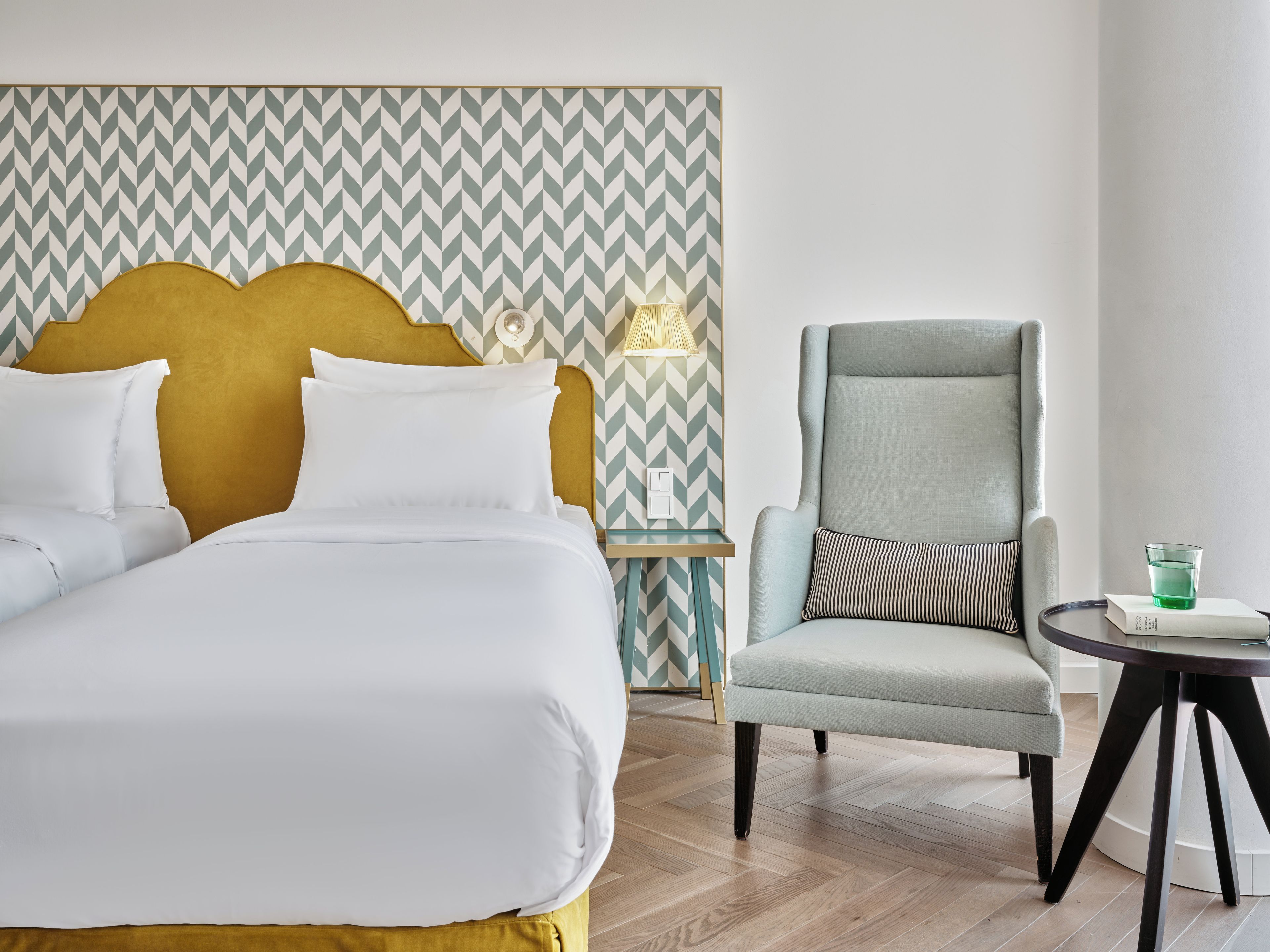 Une chambre d’hôtel avec un lit, une chaise, une table de chevet et une lampe.