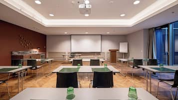 Ein Konferenzraum mit Tischen, Stühlen, einem Projektor und einer Leinwand.