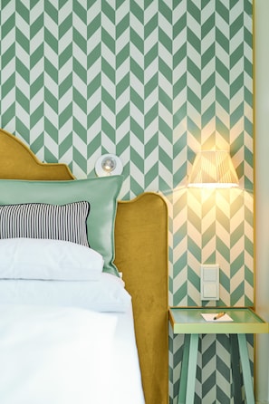 Una cama con cabecera verde y blanca estampada con un patrón de chevrón, una lámpara de noche y una mesita de noche con lámpara.