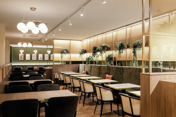 A restaurant interior with booths, tables, and hanging plants. - Crowne Plaza Vienna by IHG (Vienna)
