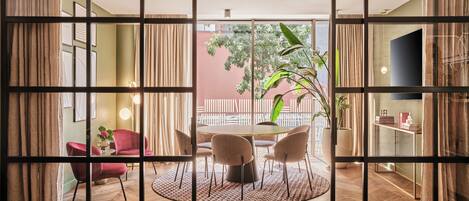Una habitación con comedor, una silla roja, una mesa redonda y vistas al exterior a través de un panel de vidrio.