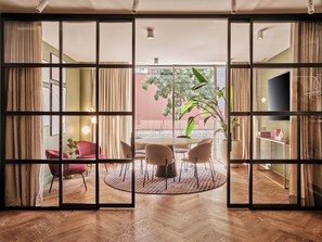 Una habitación con comedor, una silla roja, una mesa redonda y vistas al exterior a través de un panel de vidrio.