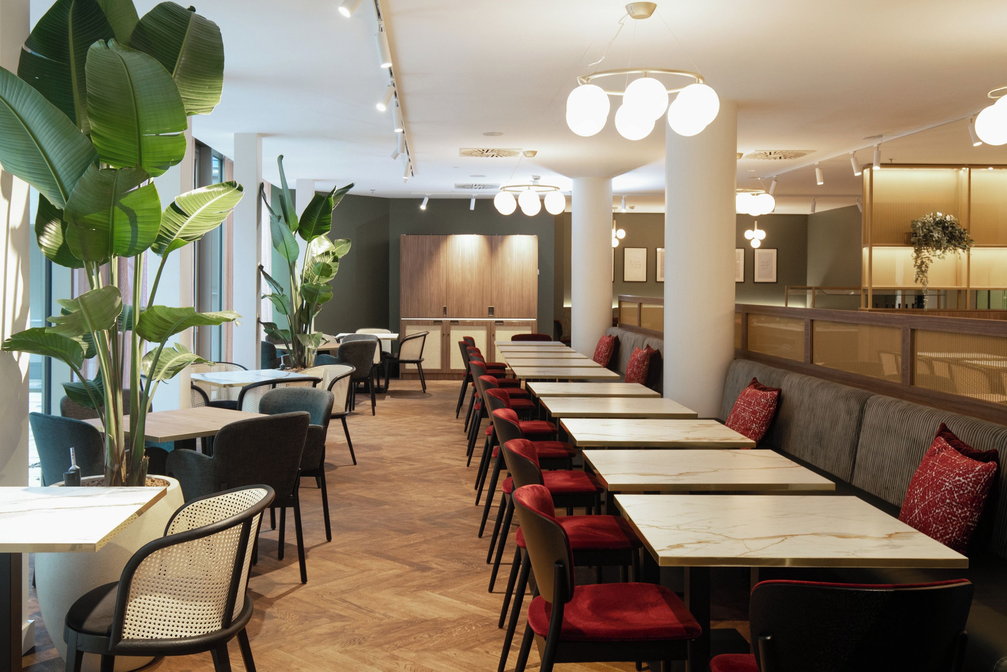 A restaurant with long tables, chairs, and potted plants.