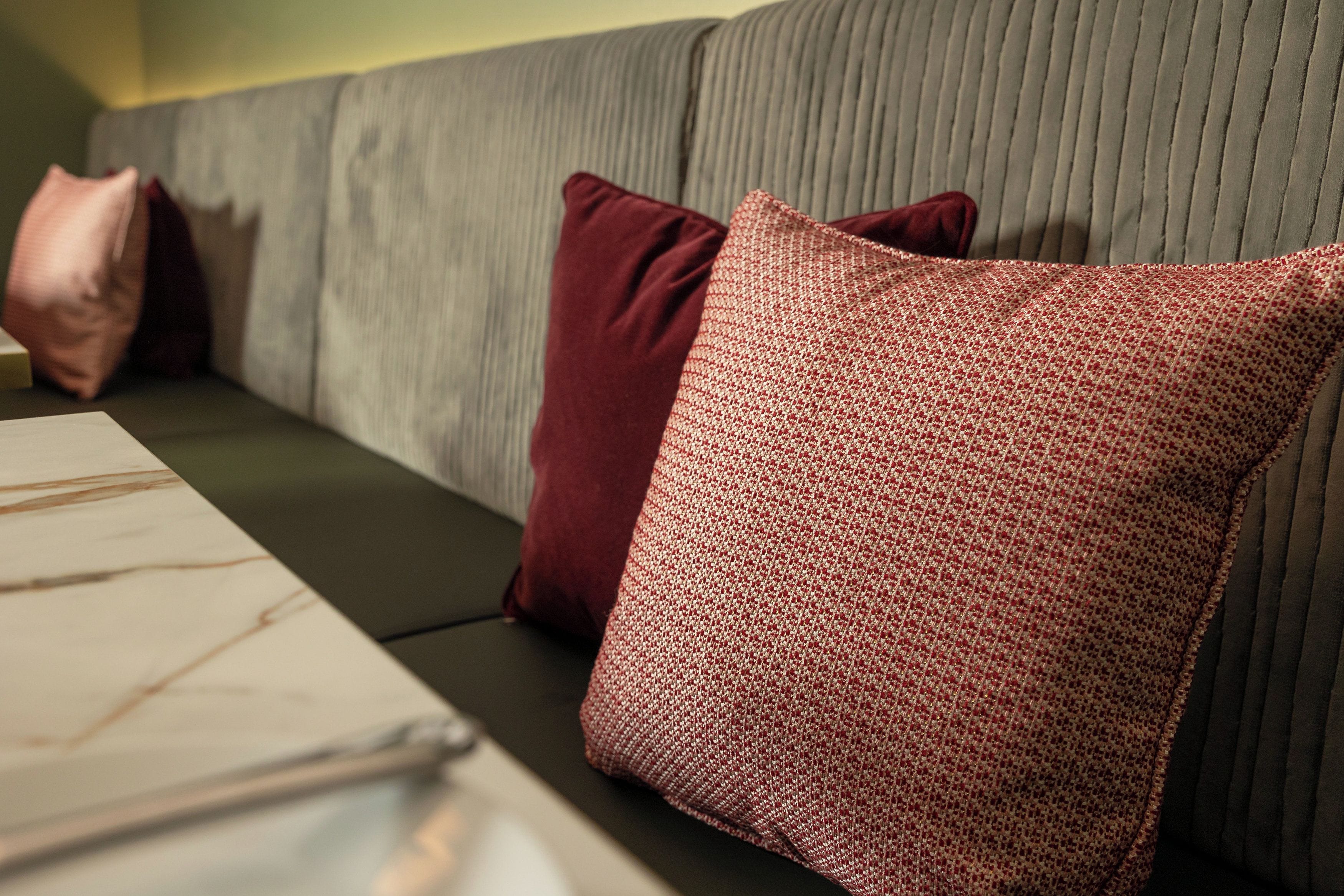 A sectional sofa with a grey upholstered backrest and two red pillows.