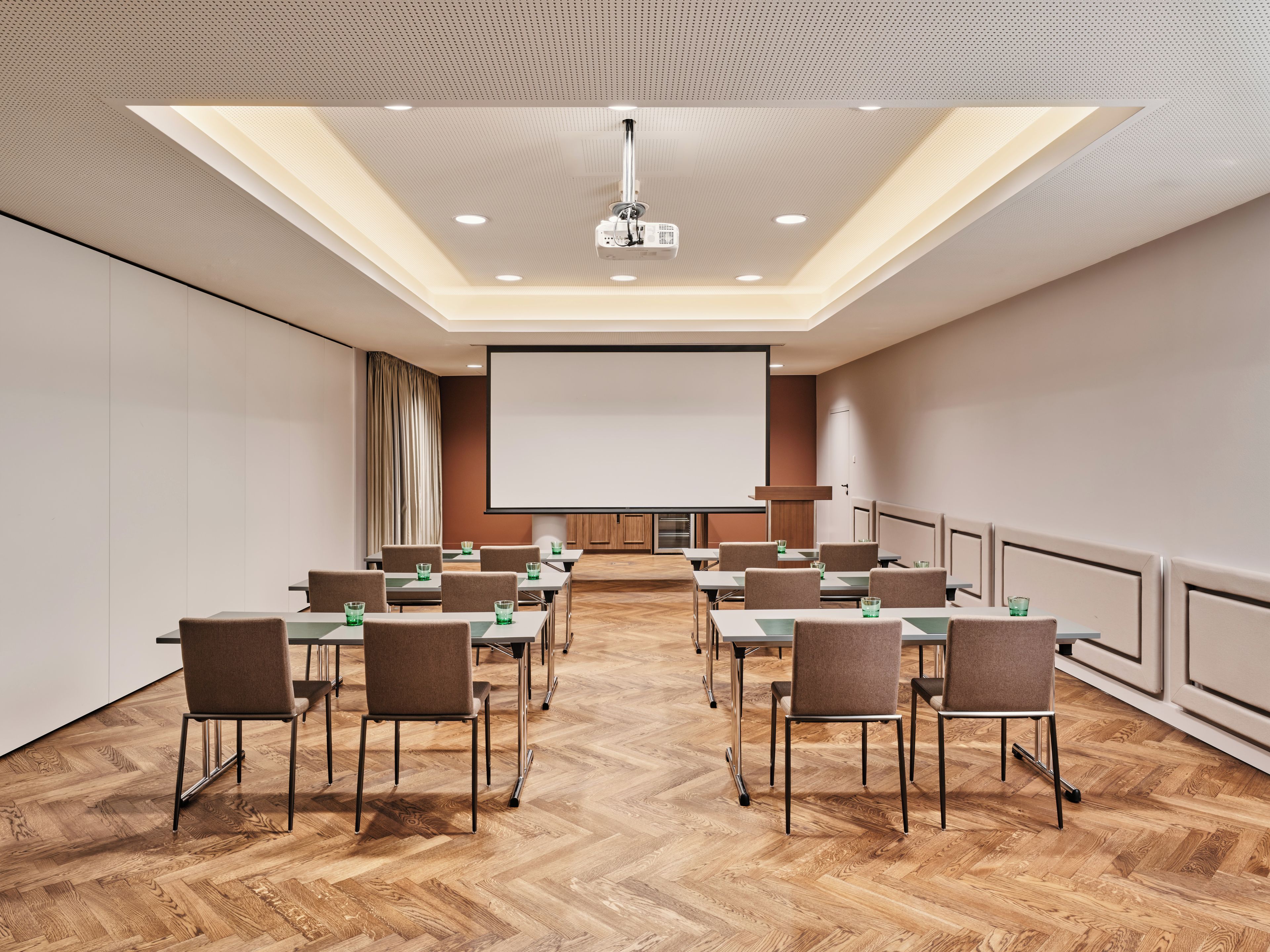 Un salón de conferencias con una pantalla grande, varias mesas y sillas dispuestas para reuniones.