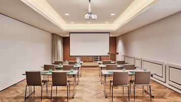 Un salón de conferencias con una pantalla grande, varias mesas y sillas dispuestas para reuniones.