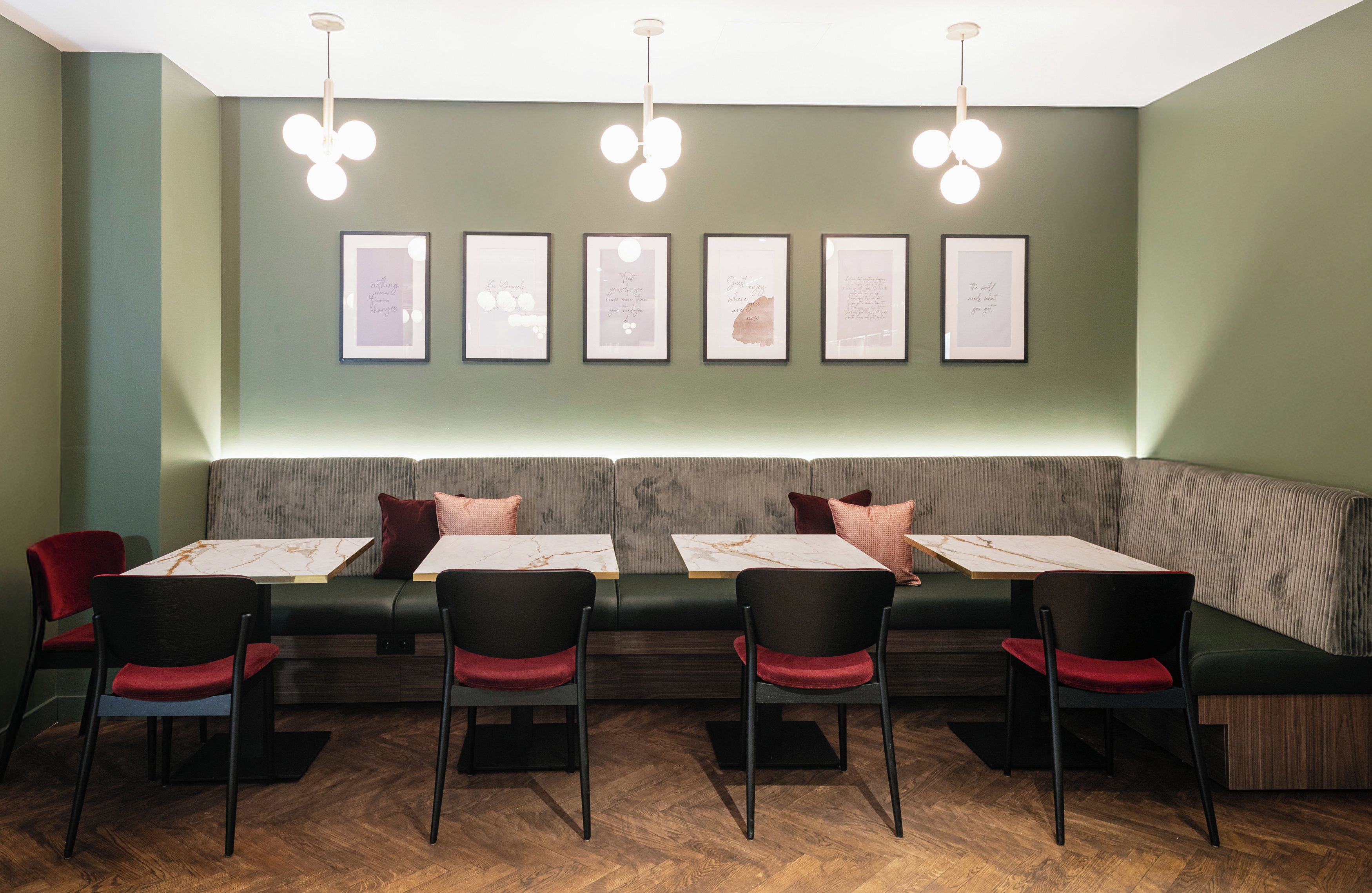 Interior de un restaurante con una larga zona de asientos tipo banco, mesas con sillas y citas inspiradoras enmarcadas en la pared.