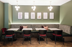 Interior de un restaurante con una larga zona de asientos tipo banco, mesas con sillas y citas inspiradoras enmarcadas en la pared.