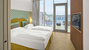 A modern hotel room with a large bed, a television, and a balcony with a city view. - MAXX by Steigenberger Vienna (Vienna)